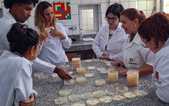 Jovens vestidos de jaleco branco em volta de uma mesa fazendo pesquisa