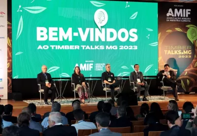 Foto de dispositivo com um painel ao fundo escrito: "Bem-vindos ao Timber Talks MG 2023". À frente dele, estão sentadas cinco autoridades, com o governador Romeu Zema ao meio.
