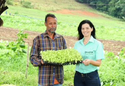 Extensionista da Emater  ao lado de um agricultor. Ambos seguram um pé de alface.