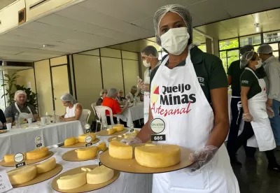 mulher segundo tabua de queijo com as mãos e uma mesa atrás dela com diversos queijos