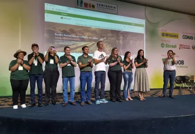 Pessoas no palco e ao fundo a projeção do site.