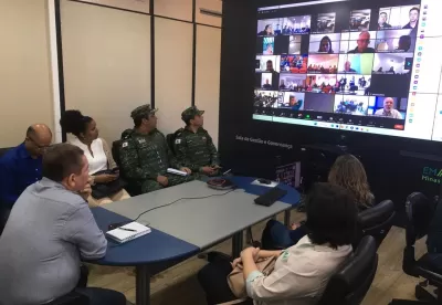 Servidores estão sentados ao redor de uma mesa, acompanhando a reunião.