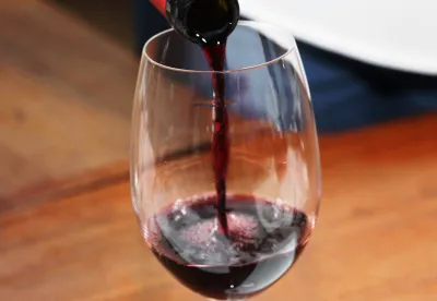 A imagem mostra uma taça sendo cheia de vinho tinto