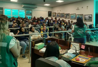 Mulheres com uniformes escrito Defesa Sanitária IMA diante de plateia. Uma deles de costas fala para a plateia.