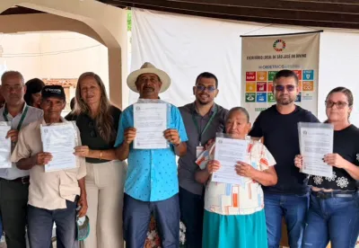 Produtores rurais segurando os títulos de Regularização da Propriedade da Terra, após receberem os documentos.