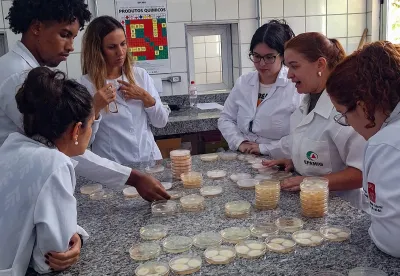 Jovens vestidos de jaleco branco em volta de uma mesa fazendo pesquisa