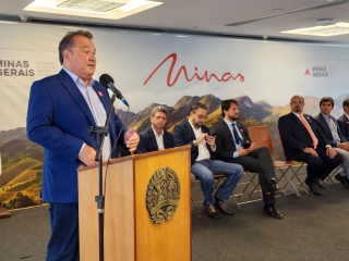 secretário de agricultura thales fernandes discursando no púlpito com o brasão de minas gerais, autoridades ao fundo sentadas, bandeira de minas gerais e do brasil do lado esquerdo e a inscrição minas ao fundo