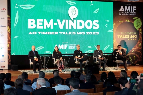 Foto de dispositivo com um painel ao fundo escrito: "Bem-vindos ao Timber Talks MG 2023". À frente dele, estão sentadas cinco autoridades, com o governador Romeu Zema ao meio. 