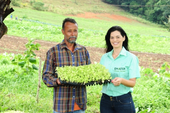 Extensionista da Emater ao lado de um agricultor. Ambos seguram um pé de alface.