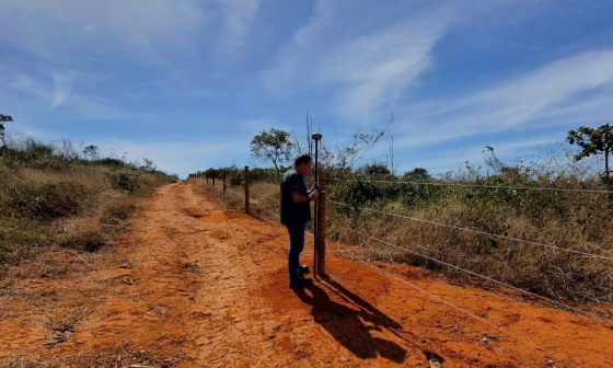 Homem vestido de preto faz medição georreferenciada em área rural.