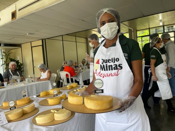 mulher segundo tabua de queijo com as mãos e uma mesa atrás dela com diversos queijos