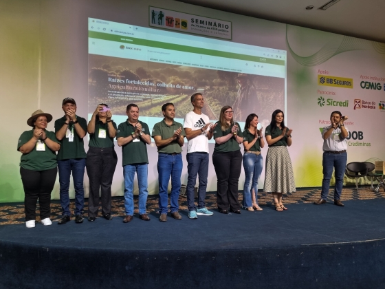 Pessoas no palco e ao fundo a projeção do site.