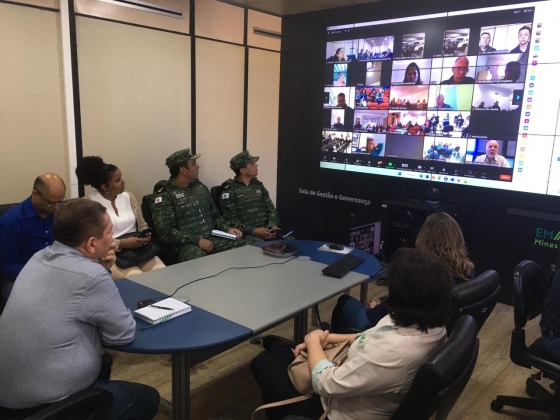 Servidores estão sentados ao redor de uma mesa, acompanhando a reunião.
