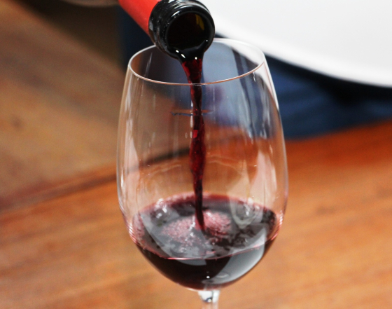 A imagem mostra uma taça sendo cheia de vinho tinto