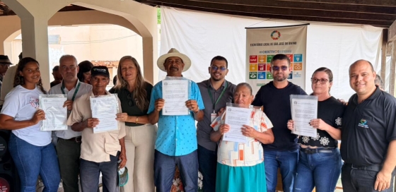 Produtores rurais segurando os títulos de Regularização da Propriedade da Terra, após receberem os documentos.